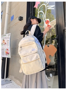 Detail view of multi-pocket white nylon backpack with decorative SUPPLYCO woven straps