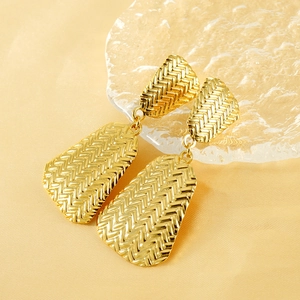 Gold geometric trapezoid drop earrings with textured herringbone pattern on silk background