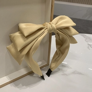 Detail of beige fabric headband featuring a triple-layered bow with soft texture