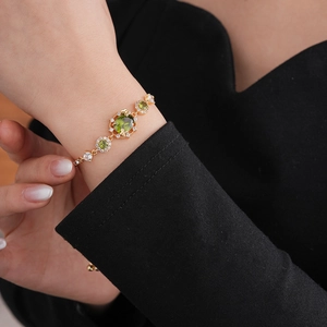 Détail d'un bracelet doré avec pierres précieuses vertes et diamants sur le poignet