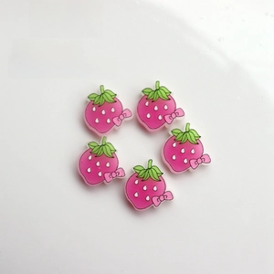 Detailed view of pink resin strawberry charms with green leaves and bows for DIY crafts