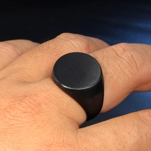 Close-up of a men's matte black stainless steel signet ring worn on a person's finger