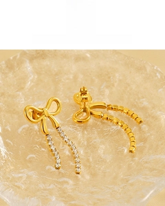 Detail of 18K gold plated bow earrings with sparkling rhinestone tassels on glass