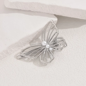 Close-up of a silver butterfly hair clip with hollow wings and inlaid pearls on stone