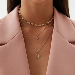 Close-up of golden layered necklace with star and moon pendants on a model in pink blazer