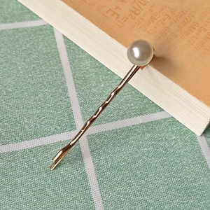 Detail of a gold metal hair clip featuring a white pearl set against a book