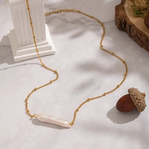 Elegant gold chain necklace featuring a baroque pearl pendant on a white marble surface
