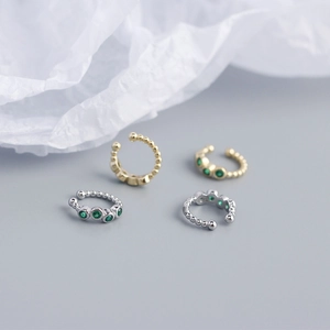 Detailed macro view of S925 silver ear cuffs in gold and silver with green gemstones