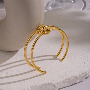 Detail eines minimalistischen Goldknoten-Armreifs auf einem weißen Steinsockel