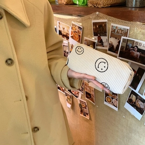 Close-up of off-white corduroy cosmetic bag with black embroidered smiley face detail