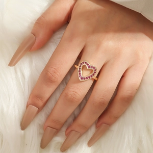 Close-up of heart-shaped gold ring set with red zircons worn on finger over plush background