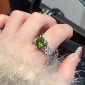 Macro detail of silver heart ring featuring a vibrant green zircon and pave diamonds