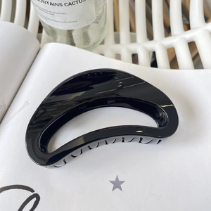 Close-up of a glossy black D-shaped hair claw clip on a white minimalist background
