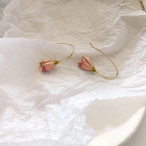 Detailed view of pink enamel tulip drop earrings on white textured background