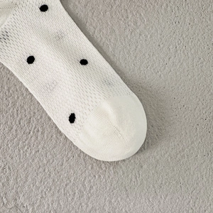 Macro detail of breathable white knit socks with black polka dot pattern on stone background