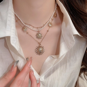 Close-up of layered necklace with pearl chain and sun face pendant on a white shirt