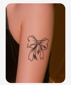 Close-up of a delicate black line bow tattoo sticker applied on woman's inner upper arm
