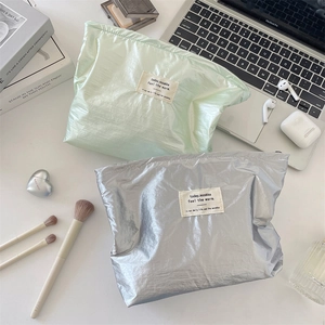 Detailed view of large silver and green makeup bags with wrinkled texture on a desk