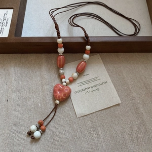 Détail du pendentif cœur en céramique fait main avec corde tressée sur un fond de lin rustique
