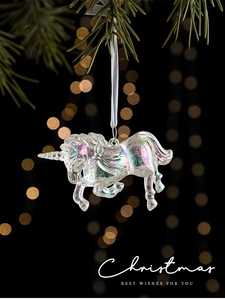 Close-up of iridescent acrylic unicorn ornament hanging on a pine tree with warm bokeh