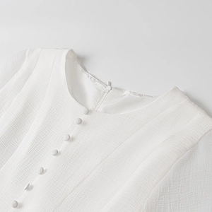 Close-up of white dress neckline with textured fabric, matching buttons and hidden zipper