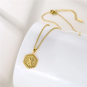 Detailed close-up of a gold hexagonal pendant with letter X on a stainless steel chain