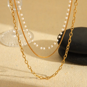 Three-layer 18K gold plated stainless steel necklace with faux pearls on beige background