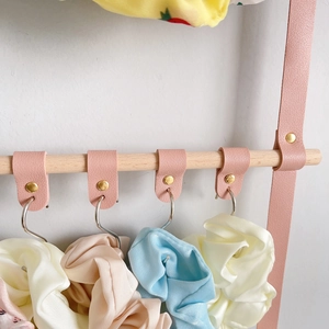 Detail of pink PU leather hanging straps on a wooden rod for hair accessory storage