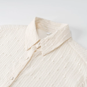 Detail of cream white shirt collar showing textured fabric with small pom-poms and size S label