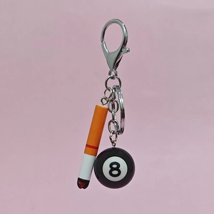 Close-up of a mini fake cigarette and black 8 pool ball charms on a metal keychain