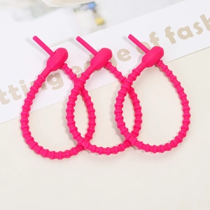 Close-up of three bright pink silicone cable ties with textured surface on a desk