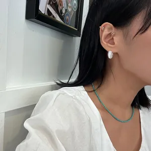 Detail showing a textured silver earring hoop and a delicate turquoise beaded necklace
