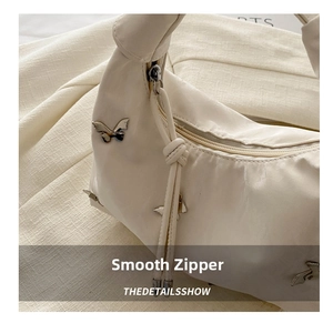 Detailed close-up of a beige hobo bag showing the smooth zipper and silver butterfly charm