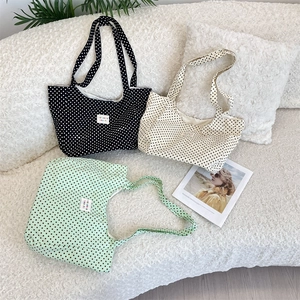 Three large polka dot canvas tote bags in black, white, and green on a soft sofa