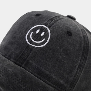 Detailed close-up of white smiley face embroidery on washed cotton baseball cap