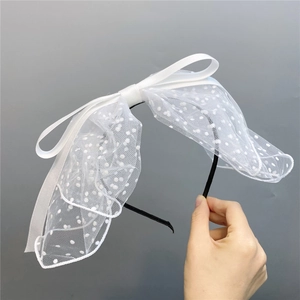 Detail of white satin bow headband with delicate polka dot tulle veil for bridal styling