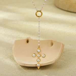 Golden stainless steel cross pendant necklace with pearl on a textured beige background