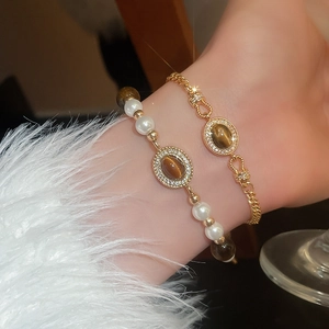 Gros plan de bracelets vintage en perles dorées et œil de chat portés au poignet