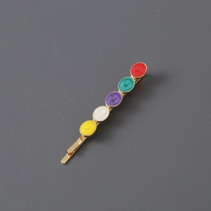 Golden rhinestone hair clip with five colorful circular resin stones on a grey surface