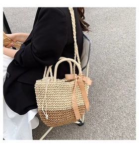 Detail of woven straw handbag featuring two-tone color block and decorative silk bow