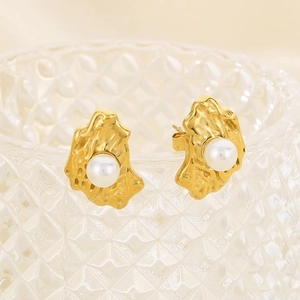 Irregular gold texture pearl earrings displayed on a glass edge with soft shadows