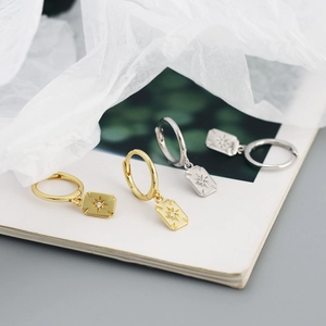 Macro shot of 925 silver hoop earrings with starburst pendants in gold and silver finish