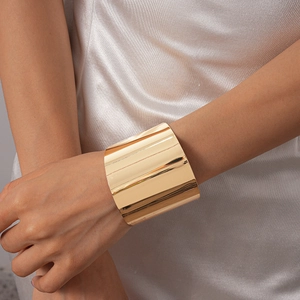 Gros plan d'un large bracelet manchette en métal doré poli sur un mannequin en satin