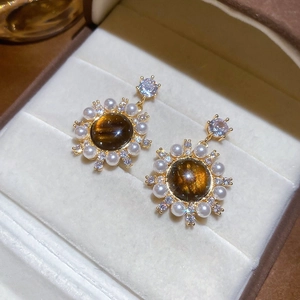 Detailed shot of tiger eye earrings with pearls and crystals in a beige jewelry box