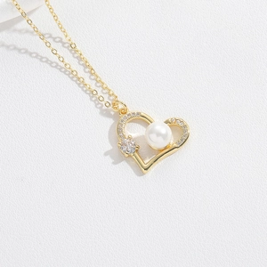 Close-up of golden hollow heart pendant with a white pearl and sparkling rhinestones