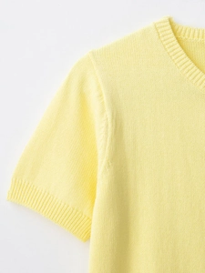 Macro shot of light yellow knit top featuring ribbed crew neck and sleeve cuffs detail