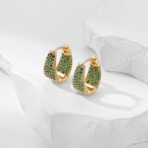 Elegant gold hoop earrings with green zircon pavé stones displayed on a white stone base