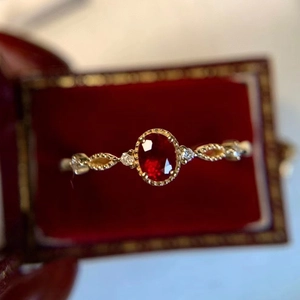 Classic vintage gold ring with oval red gemstone and diamonds on dark velvet box