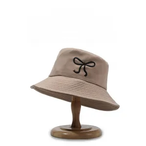 Detailed embroidery of a black bow on a beige cotton sun hat with a clean white background