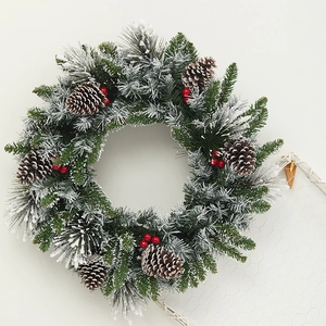 Christmas wreath with artificial pine needles, white snow frost, pine cones and red berries